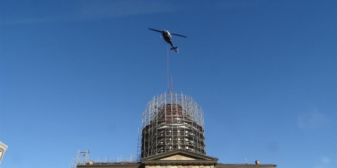 A helicopter is used to remove the flagpole from atop the Old State Capitol in Springfield on Monday morning as part of a renovation project to reinforce the dome and repair a leaky roof. (Capitol News Illinois photo by Peter Hancock)