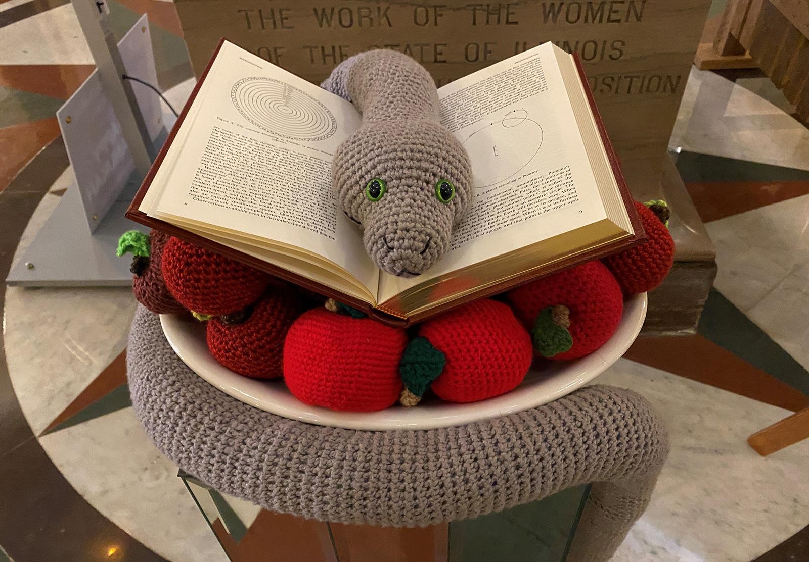 crocheted snake sitting on a book and a pile of apples