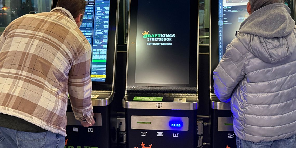 Two individuals standing in front of betting kiosks
