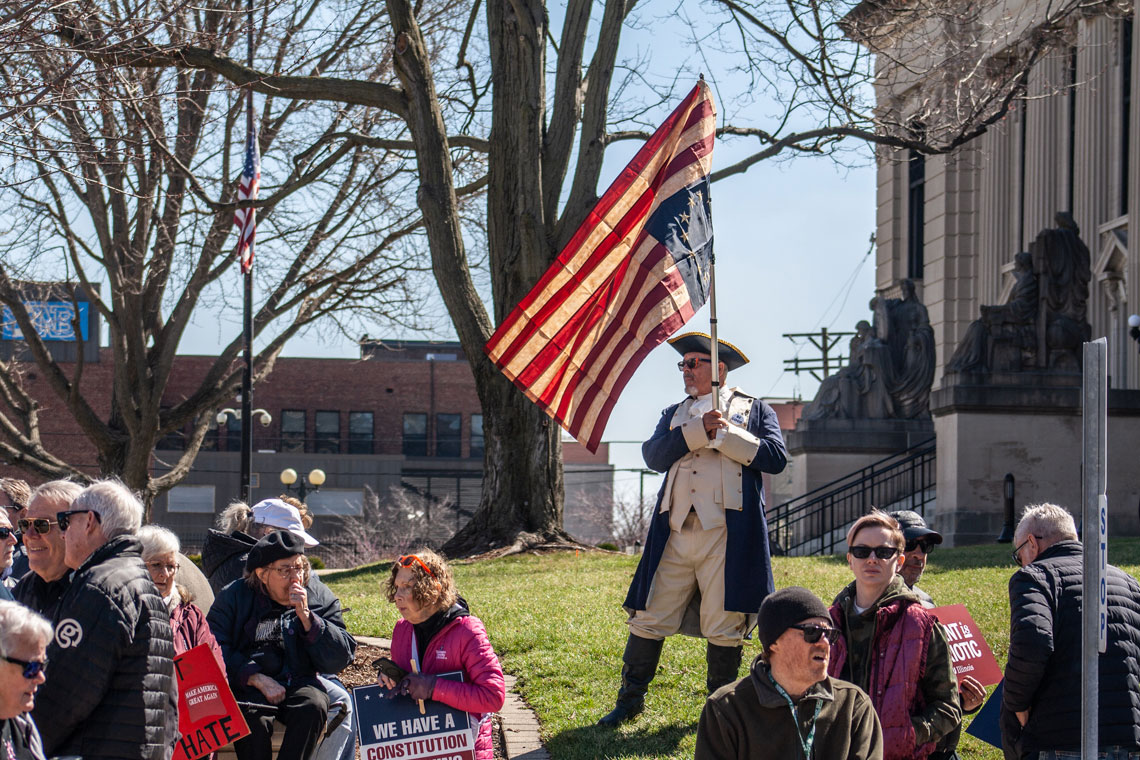 Man in Revolutionary War-era outfit holds upside-down Betsy Ross Flag