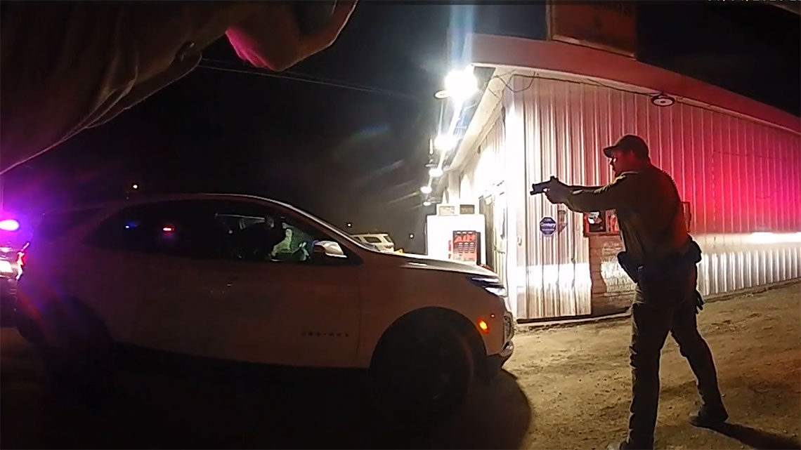Police hold firearm in front of a white vehicle