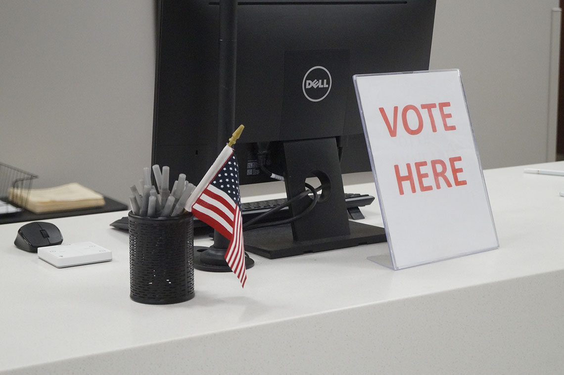Vote here sign in front of a computer monitor.
