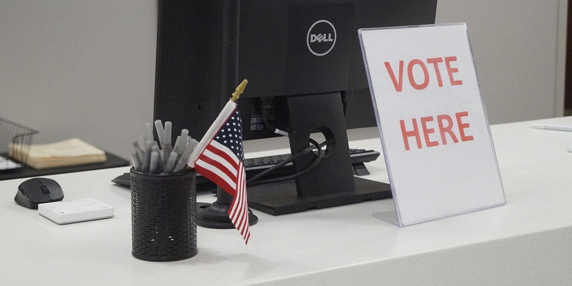 Vote here sign in front of a computer monitor.